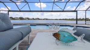 A poolside area with a view of a lake, a glass fish sculpture, and two lounge chairs. - Blue Marlin | Lake front | Pool | Panorama Screen (Port Charlotte)