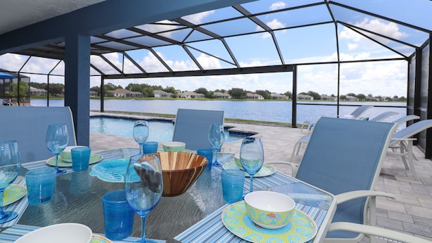 An outdoor dining area with a view of a lake and houses in the background. - Blue Marlin | Lake front | Pool | Panorama Screen (Port Charlotte)