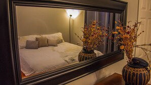 Een slaapkamer met een grote spiegel, een bed met kussens, en twee vazen met gedroogde bloemen op een nachtkastje.