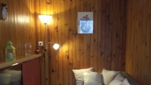 A cozy living room with wooden walls, a grey sofa with pillows, a wooden coffee table, a TV, and a floor lamp. - Mökki "the Ann the Annonciade" (LE LUC)