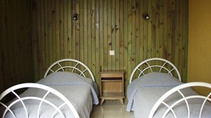 A room with two single beds, each with a metal frame and grey bedding. There is a small wooden nightstand between the beds. The walls are paneled with vertical wooden slats. - Mökki "the Ann the Annonciade" (LE LUC)