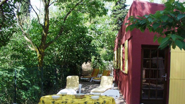 An outdoor seating area with a table covered in a yellow tablecloth, surrounded by white chairs. - Mökki "the Ann the Annonciade" (LE LUC)