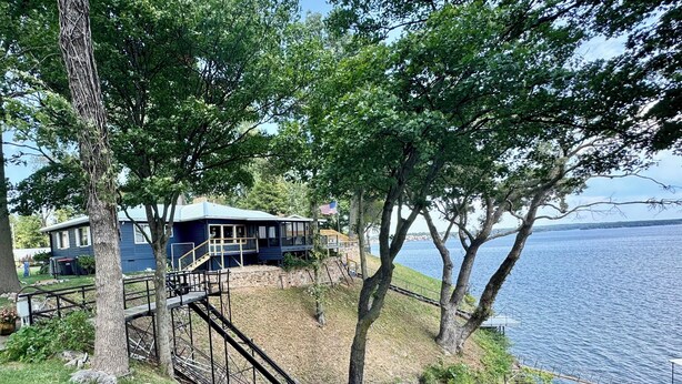 Una propiedad frente al lago con una casa, un muelle y una escalera que lleva a una terraza.