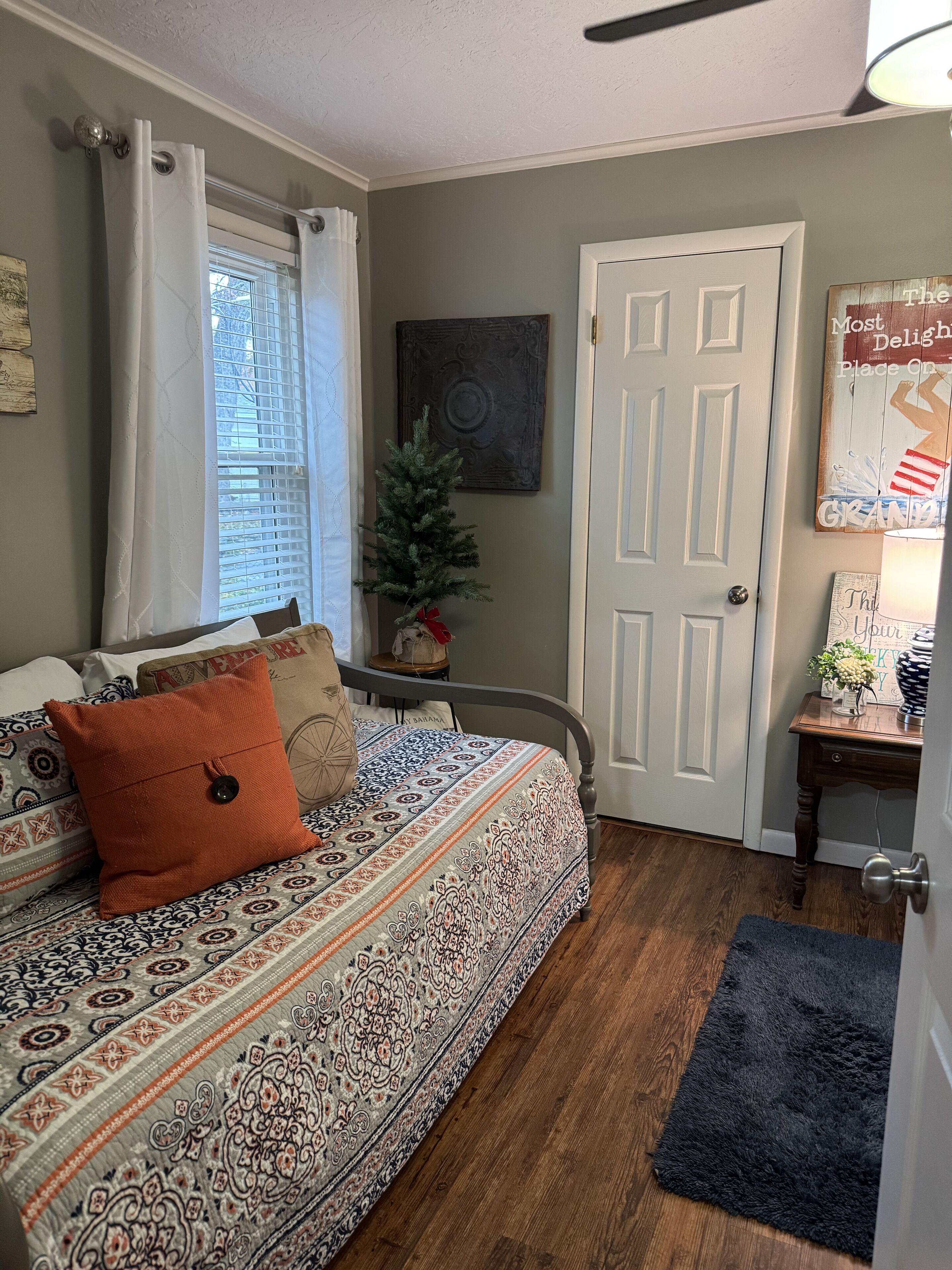A bedroom with a patterned bedspread, a small Christmas tree, and a door with a sign.