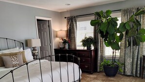 Un dormitorio con cama, cómoda, planta en maceta, silla y ventilador de techo.