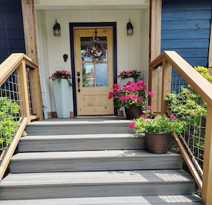 Una escalera de madera que lleva a una puerta principal con un arreglo floral y un buzón.