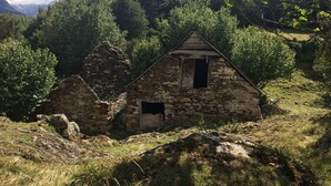 Een stenen vakantiehuisje met een puntig dak, omgeven door een dicht bos en bergen.