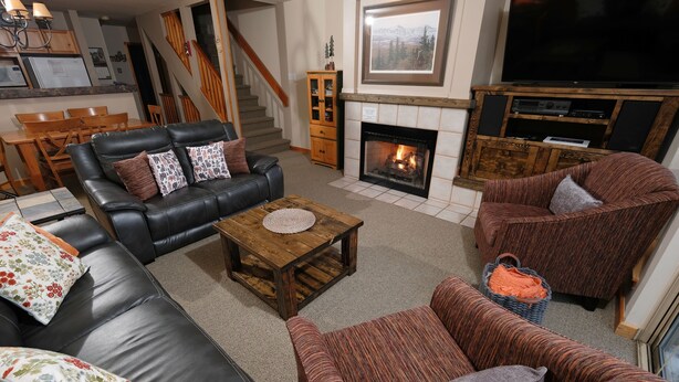 A living room with a fireplace, a television, and a dining area with a staircase. - Very Attractive Spacious Condo.  Excellent Location.  Must See! (Whistler)
