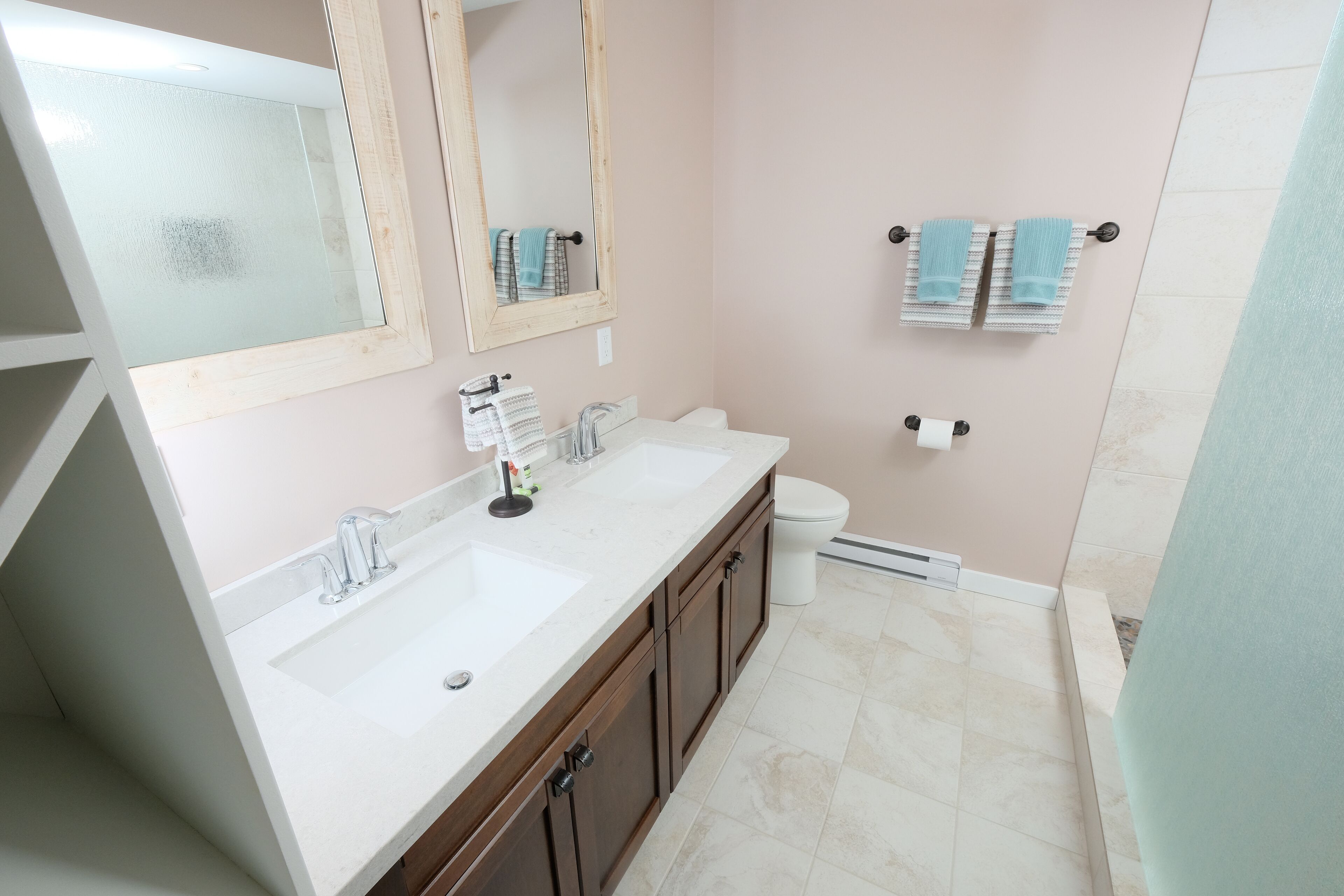A bathroom with a white sink, double mirrors, a toilet, and a towel rack with towels.