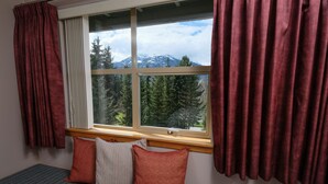 A room with a window overlooking a snowy mountain and forest. There is a bench with cushions and a wooden ledge beneath the window. - Very Attractive Spacious Condo.  Excellent Location.  Must See! (Whistler)