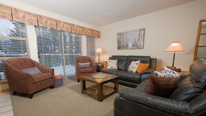 A living room with a brown armchair, a black leather sofa, a wooden coffee table, and two floor lamps. - Very Attractive Spacious Condo.  Excellent Location.  Must See! (Whistler)