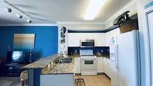 A kitchen with white cabinets, a granite countertop, a microwave, an oven, and a refrigerator. - Beachfront w/ Gulf View | 4th Floor | Elegantly Cleaned | Free WiFi |  (Panama City Beach)