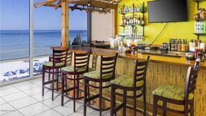 A beachside bar with wooden chairs and a bar counter, a TV mounted on the wall, and a view of the ocean. - Beachfront w/ Gulf View | 4th Floor | Elegantly Cleaned | Free WiFi |  (Panama City Beach)