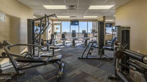 A gym with various exercise equipment, a carpeted floor, and large windows offering a view. - Beachfront w/ Gulf View | 4th Floor | Elegantly Cleaned | Free WiFi |  (Panama City Beach)