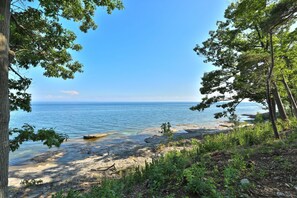 A coastal landscape with a clear view of the sea, surrounded by trees and rocky terrain.