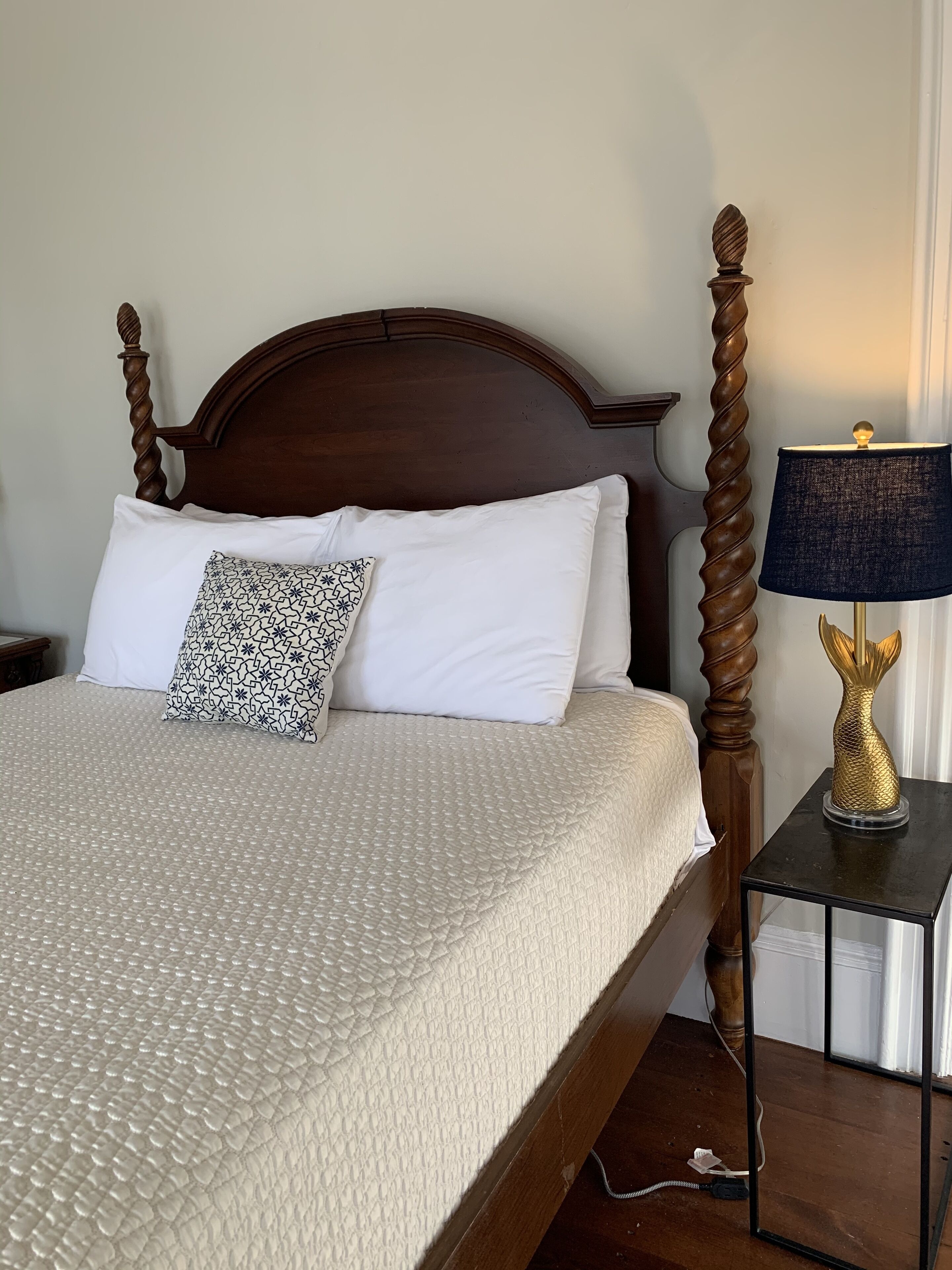 A neatly made bed with a patterned pillow, a dark wooden headboard, and a bedside table with a lamp.