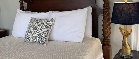 A neatly made bed with a patterned pillow, a dark wooden headboard, and a bedside table with a lamp.