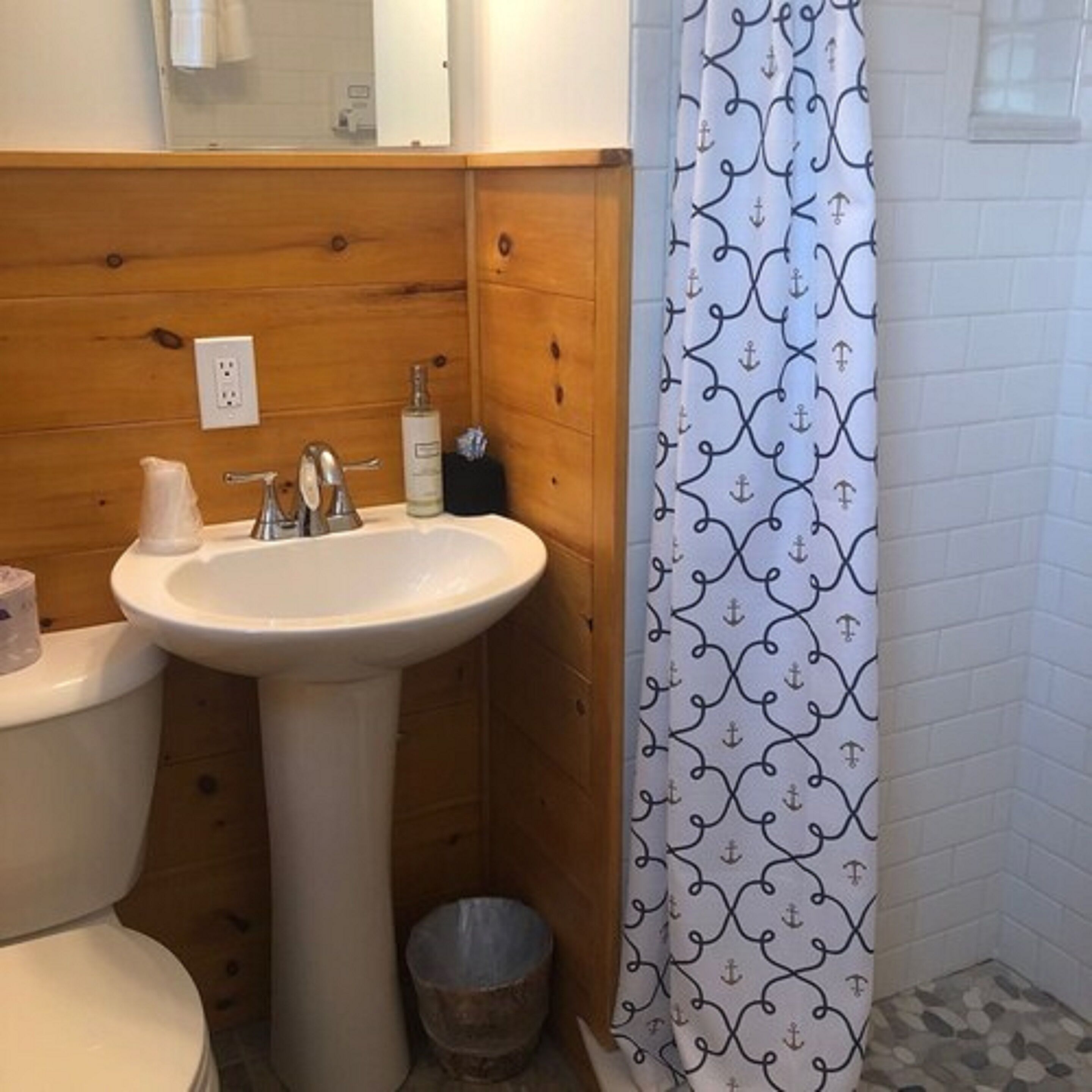 Un baño con tocador de madera, un lavabo blanco y cortina de ducha con estampado de anclas.