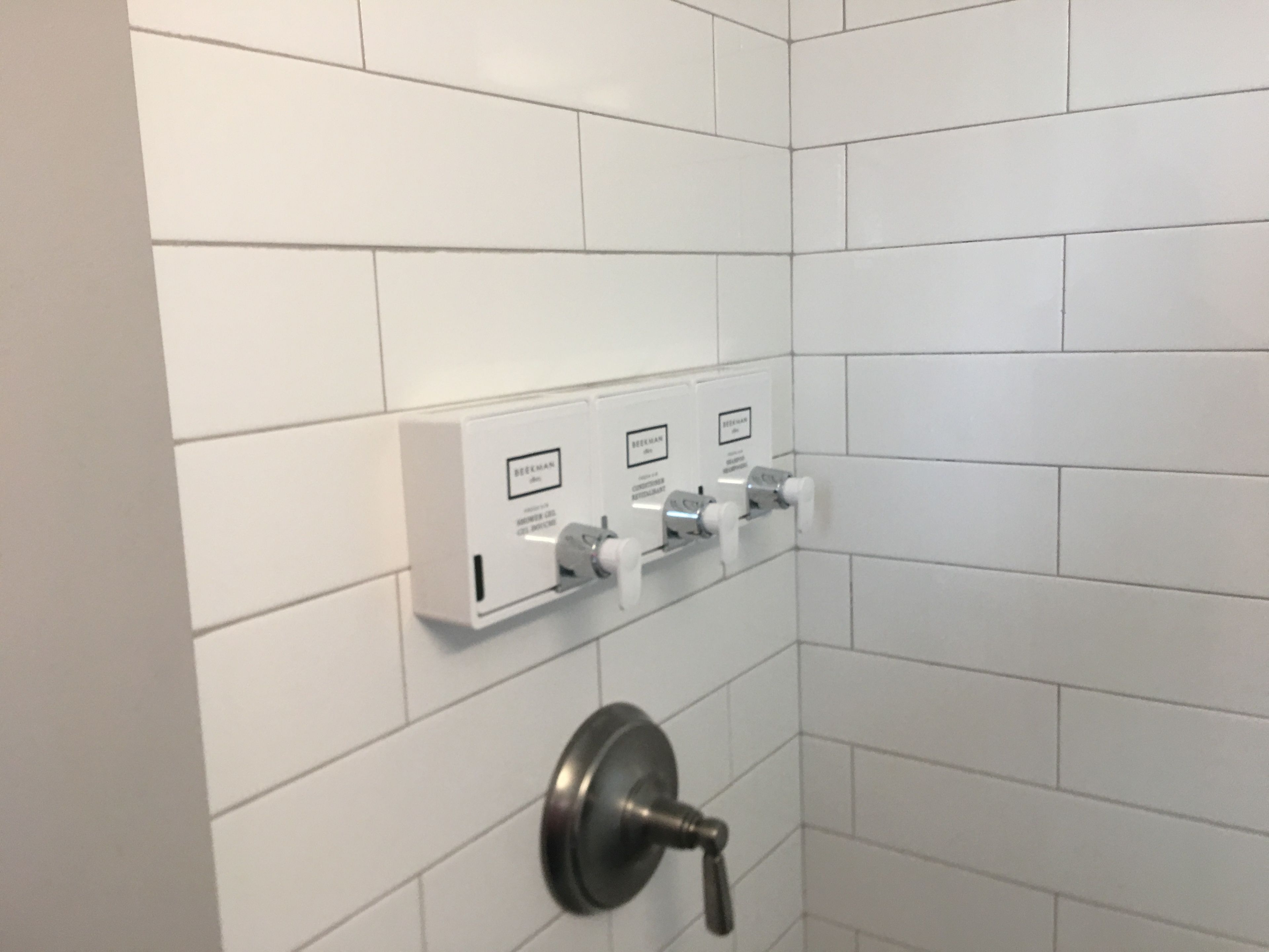 A bathroom with white tiled walls and a wall-mounted sink with a faucet.