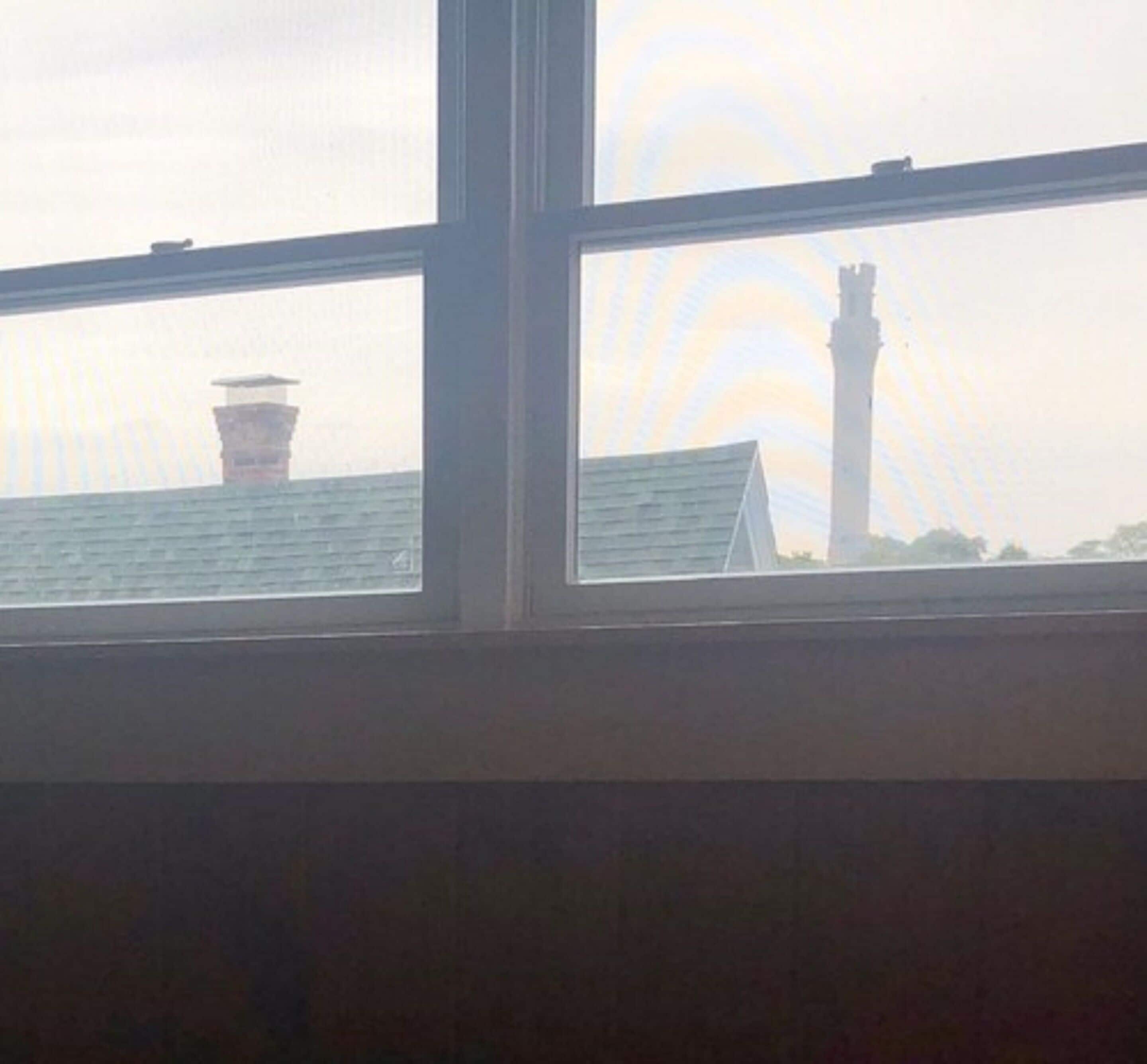 A view through a window with a building's roof and chimney in the background.