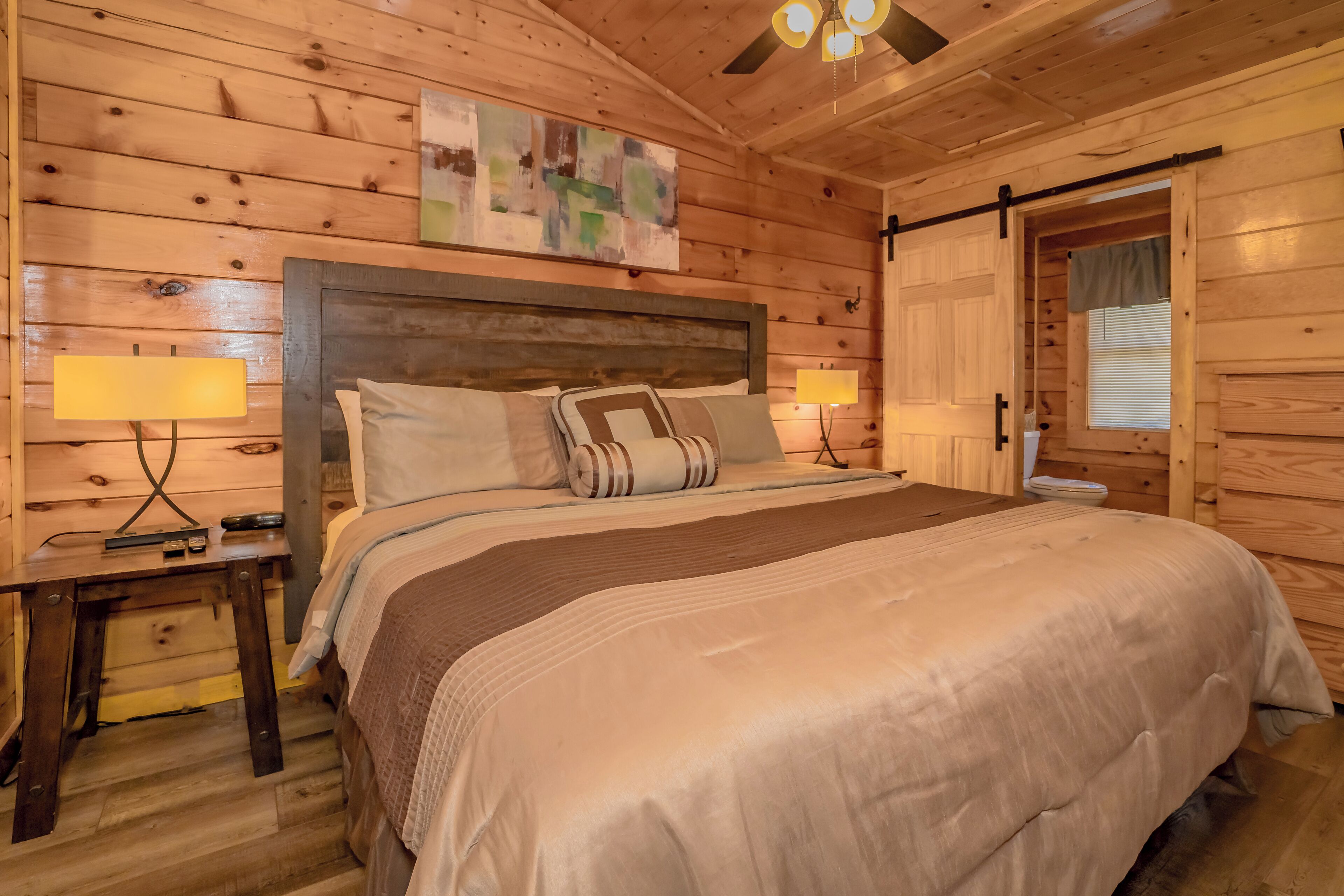 Une chambre située dans une cabane en bois, avec un grand lit, deux lampes de chevet, un ventilateur de plafond et une porte coulissante de style grange.