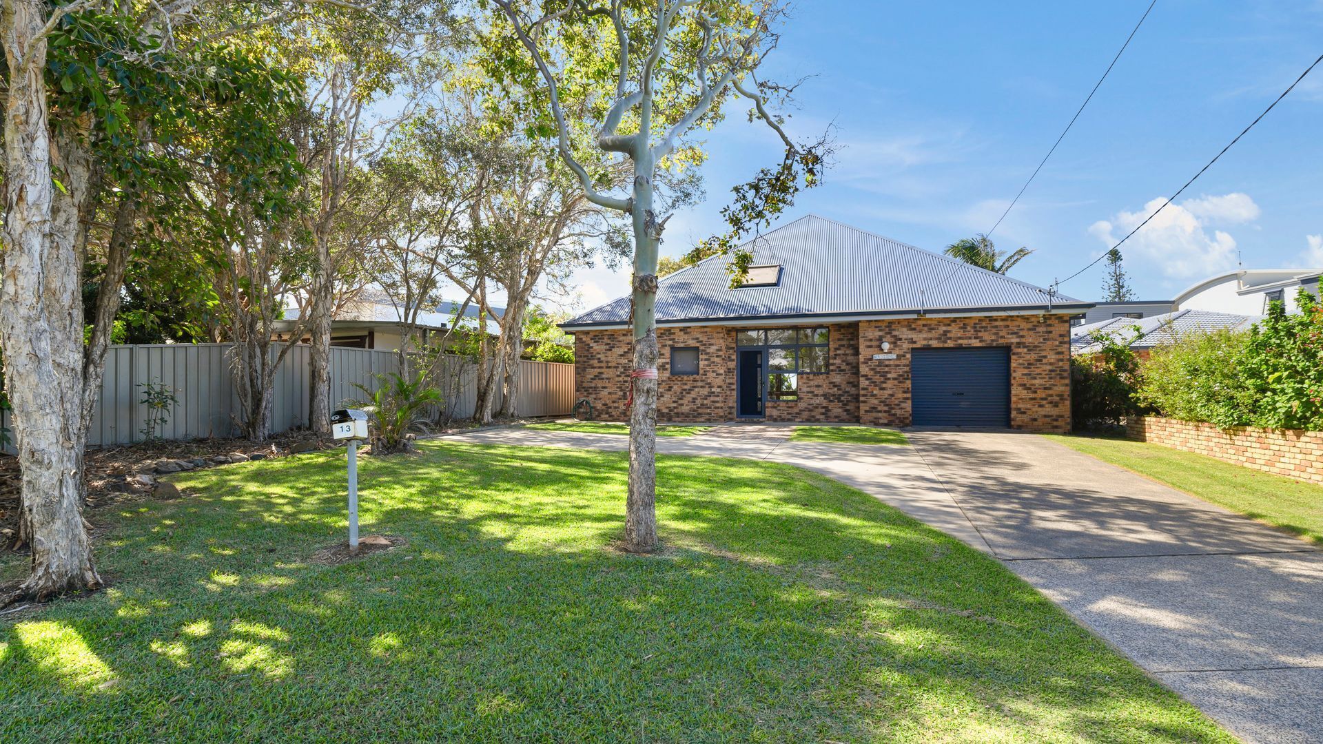 A residential house with a brick exterior, a metal roof, and a front yard with a tree and mailbox.