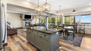 Une cuisine spacieuse dotée d’un îlot central, un coin repas avec une grande table et des chaises, et un coin salon confortable avec une cheminée.