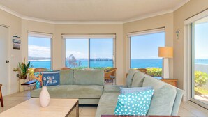 A living room with a large window offering a sea view, a sofa with patterned cushions, and a small table with a vase.