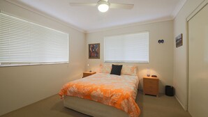 A bedroom with a bed, two nightstands, a ceiling fan, and two windows with blinds.