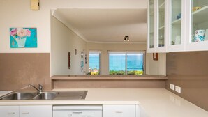 A kitchen with a view of the ocean, a sink, and cabinets.