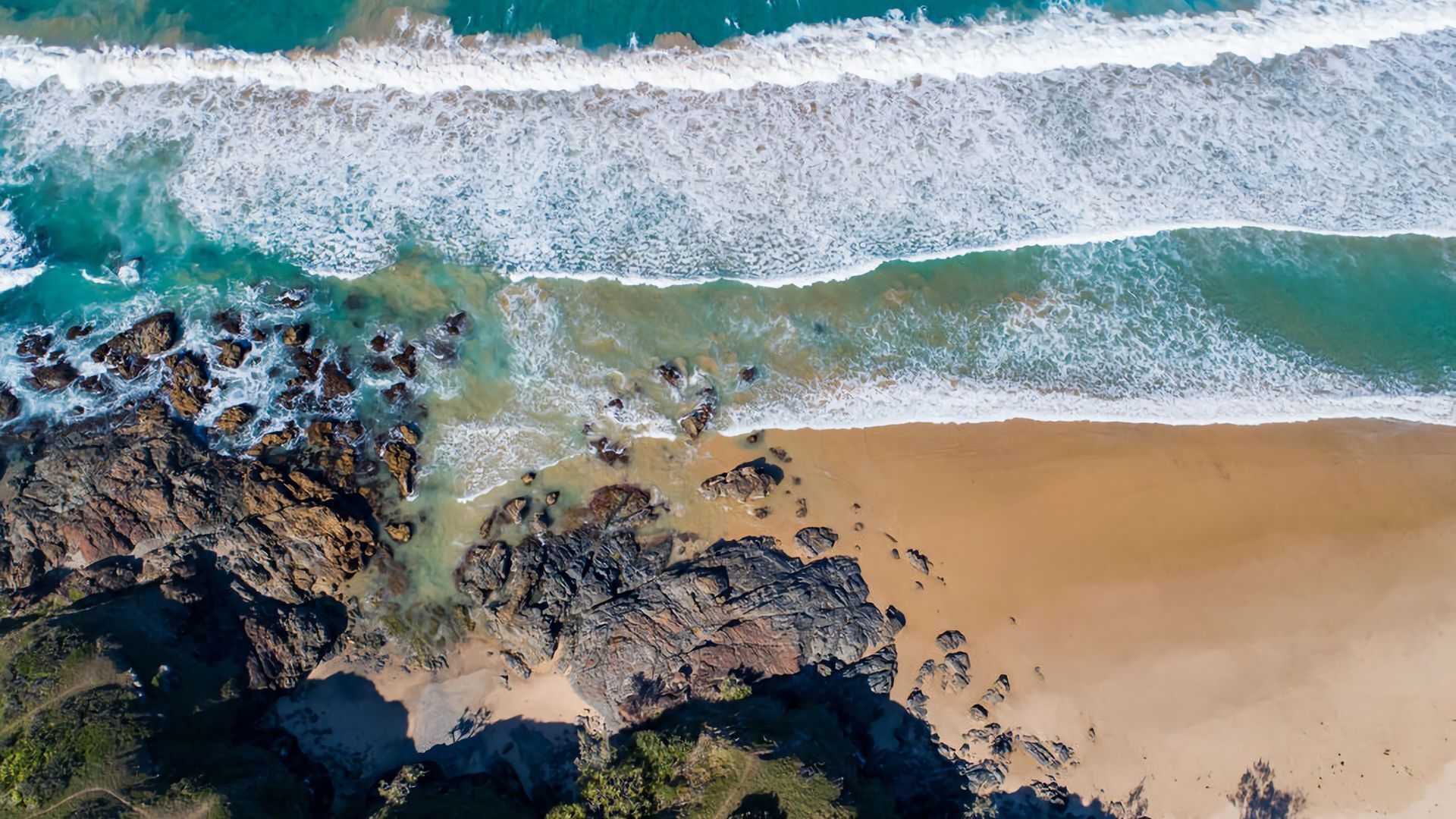 Vue aérienne d’une plage avec des formations rocheuses et une eau turquoise cristalline.