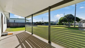 A covered outdoor area with a view of a residential street, a wooden fence, and a grassy lawn. - Len's Retreat - relax in Red Rock (Red Rock)
