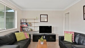 A living room with two black leather sofas, a coffee table, a TV, and a bookshelf with books and a 'WELCOME' sign. - Len's Retreat - relax in Red Rock (Red Rock)