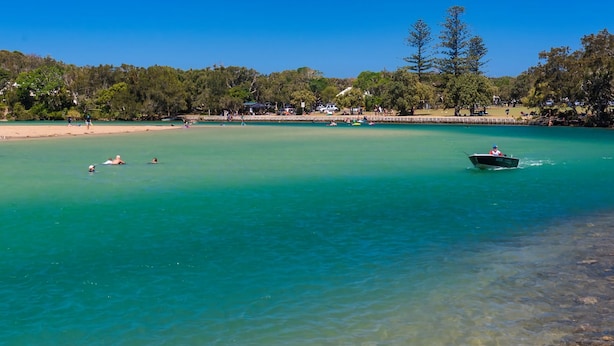 A clear turquoise sea with a boat in the distance, a sandy beach, and a forested area in the background. - Len's Retreat - relax in Red Rock (Red Rock)