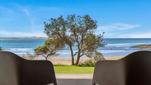 Blick auf einen Strand mit zwei Stühlen, die zum Meer zeigen, einem Baum im Vordergrund und einem klaren Himmel.