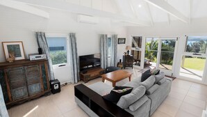 Amplio salón con televisor, sofá, mesa de centro y vistas a un jardín a través de grandes puertas correderas.