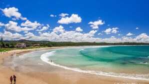 A beach with clear turquoise waters, a sandy shore, and a few people walking. - Jambi Ocean View - oceanfront Woolgoolga (Woolgoolga)