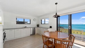 A modern kitchen with white cabinets, a wooden dining table, and a view of the ocean. - Jambi Ocean View - oceanfront Woolgoolga (Woolgoolga)