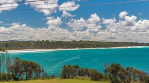 A coastal landscape with a clear view of the ocean, a sandy beach, and a forested area.