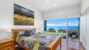 Un dormitorio con una cama grande, vistas al mar y una silla junto a la ventana.
