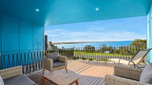 Un espacio exterior techado con mobiliario de mimbre, una mesa de madera y vista al mar.