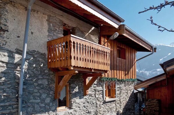 A wooden chalet with a balcony, stone walls, and a mountain view. - Mountain village apartment overlooking 3 Valleys (Montagny)