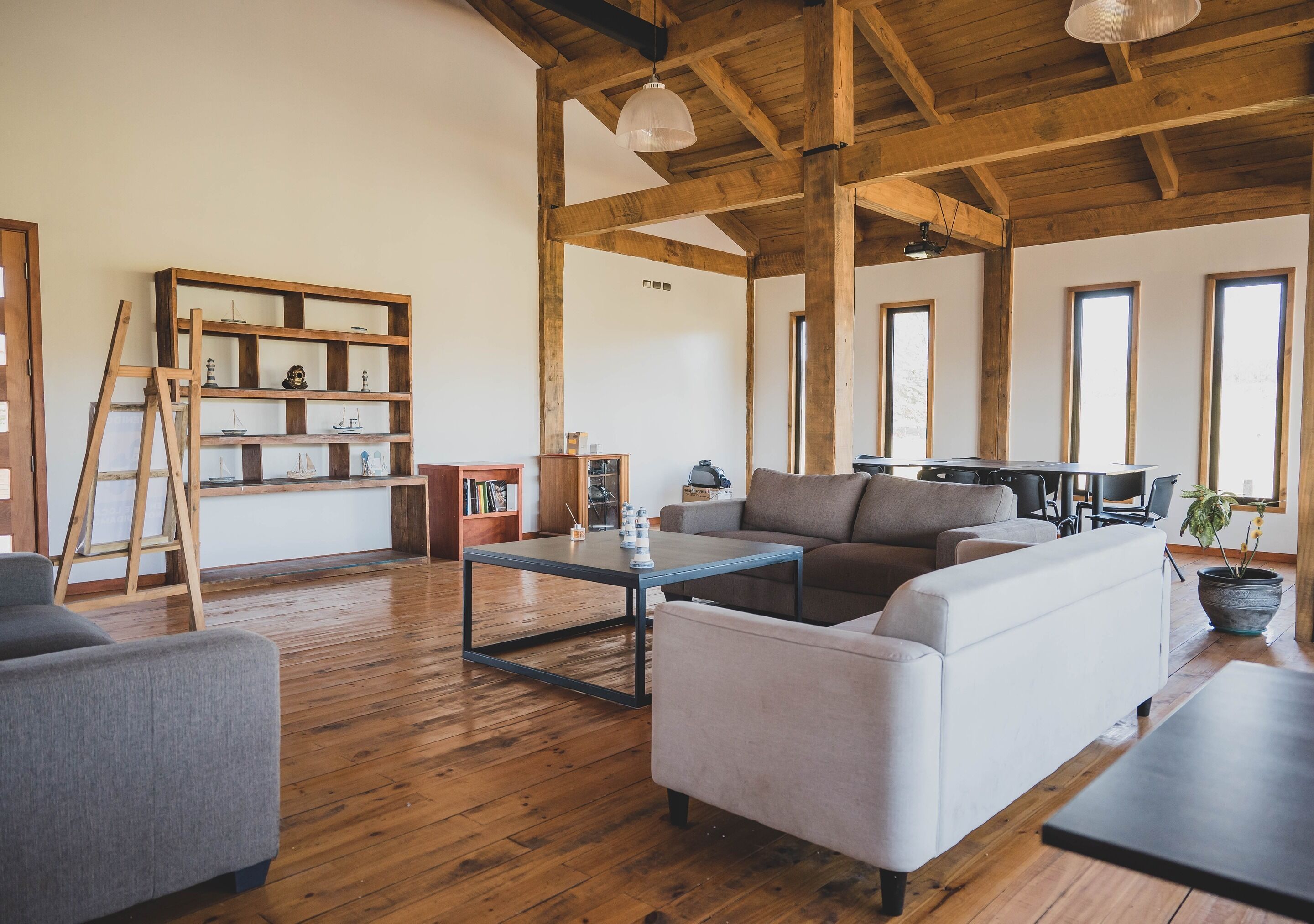 A spacious living room with wooden floors, a white sofa, a grey armchair, and a coffee table. There is a bookshelf with decorative items and a ladder leaning against it.