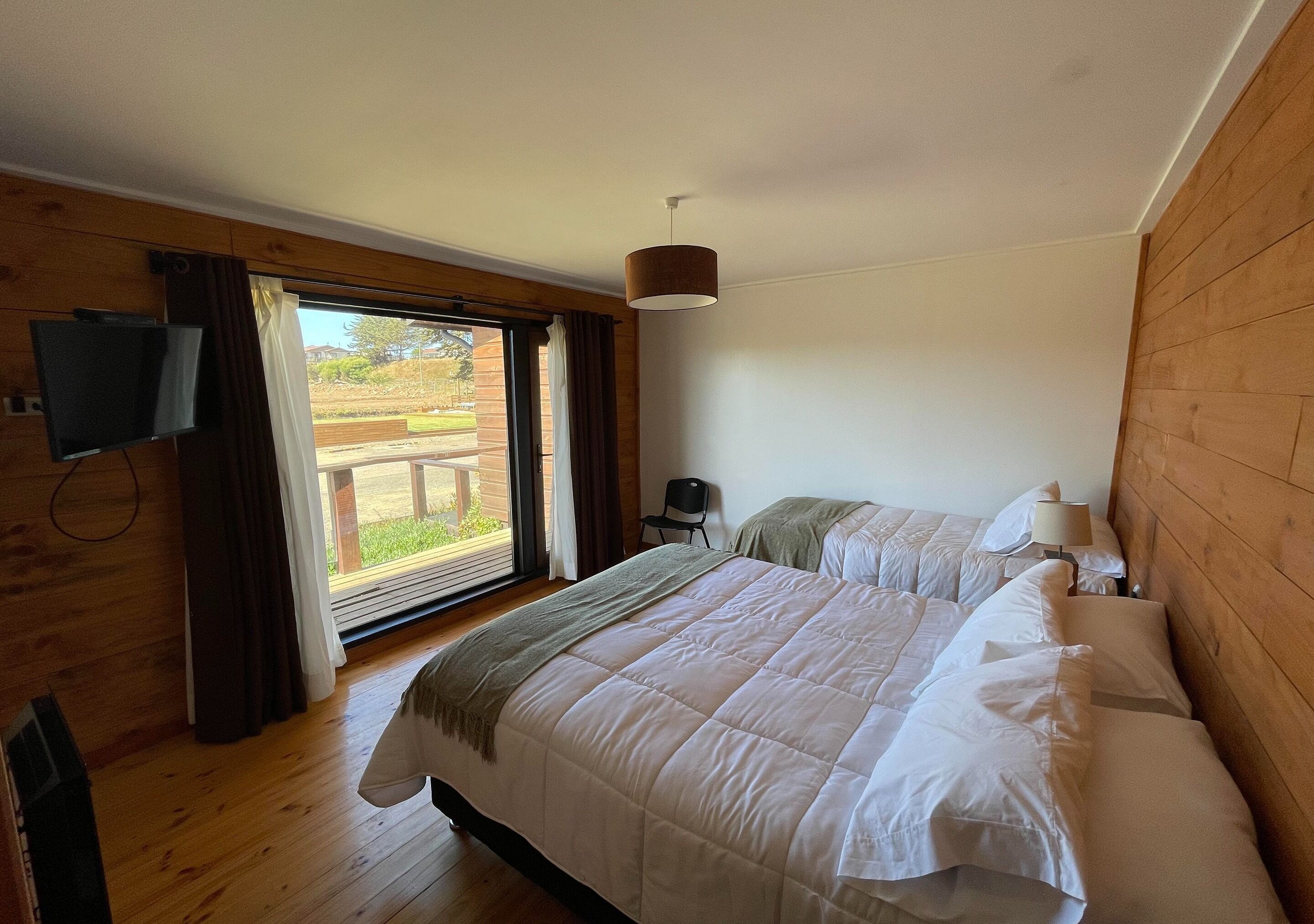 A bedroom with two beds, a TV, and a view of the outdoors.