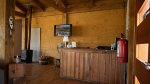 A wooden cabin interior with a wooden bar, a fireplace, a fan, and a fire extinguisher. - Hotel Puerto Madera (Pelluhue)