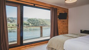 A bedroom with a large window, a bed, and a wooden ceiling. - Hotel Puerto Madera (Pelluhue)
