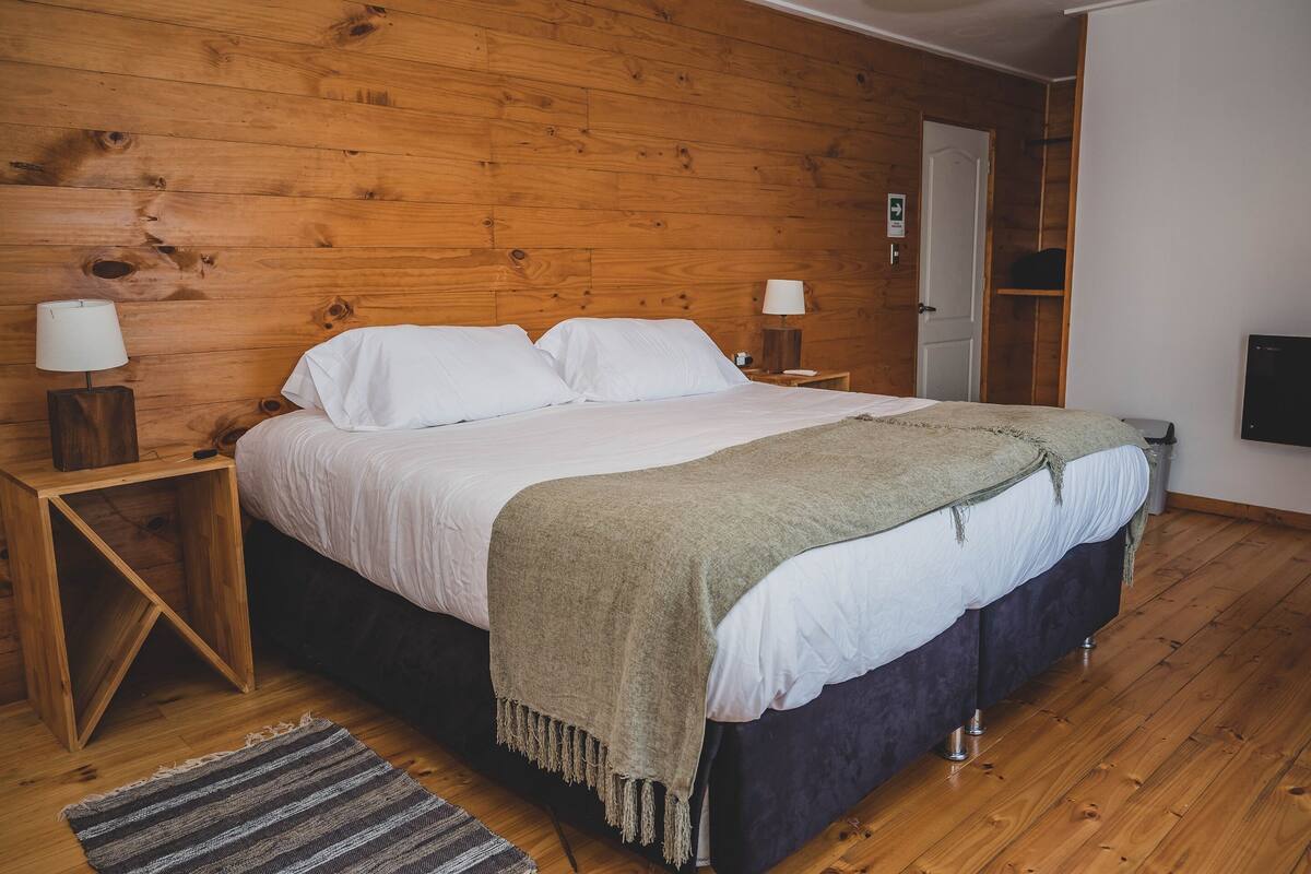 Ein Schlafzimmer mit Holzwänden, einem Bett, zwei Nachttischen mit Lampen, einem Teppich und einer Tür.