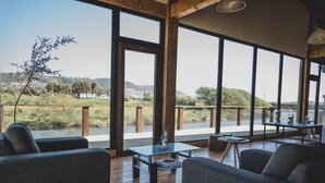 A spacious room with large windows, wooden flooring, and modern furniture including sofas and a coffee table. - Hotel Puerto Madera (Pelluhue)