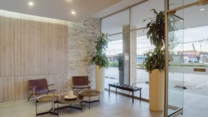 A lobby with two leather chairs, a round table, a bench, and large potted plants. - Captain's Cove (Concon)