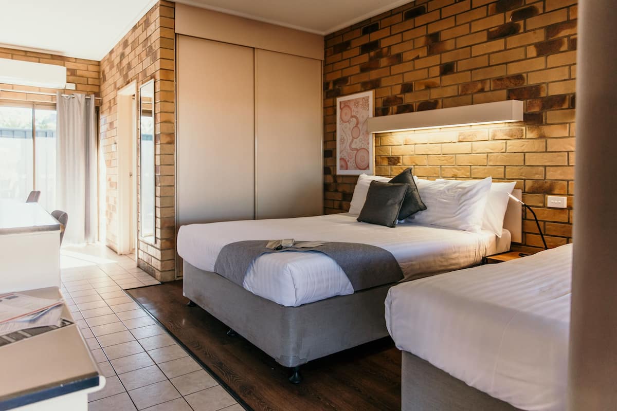 A bedroom with a brick wall, a bed with white bedding, a grey sofa, and a sliding door leading to a balcony.